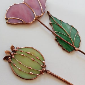May include: Two stained glass floral decorations with copper wire accents. One flower is pink and the other is green.