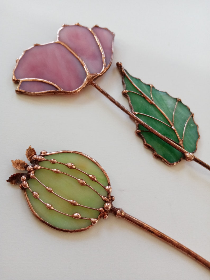 May include: Two stained glass floral decorations with copper wire accents. One flower is pink and the other is green.