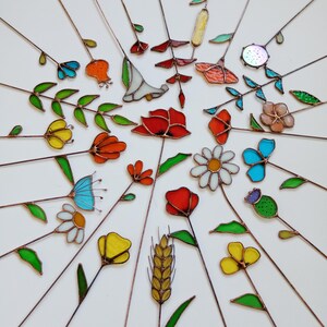 May include: A collection of colorful stained glass flowers and leaves with copper stems arranged in a radial pattern. The flowers include red poppies, yellow tulips, and blue daisies. The glass has various textures and colors.