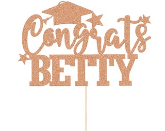 May include: Rose gold glitter cake topper with the text "Congrats Betty" and a graduation cap.