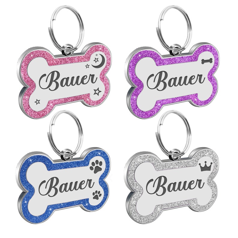 May include: Four silver bone-shaped dog tags with different colored glitter borders. The tags have the name "Bauer" engraved on them and each has a different design: a crescent moon and stars, a bone, a paw print, and a crown.