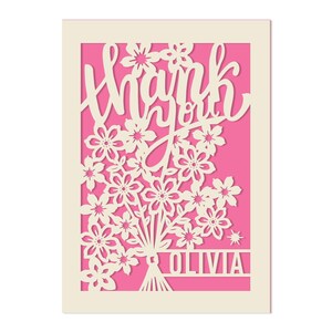 May include: A white card with a pink background and a cut-out design of flowers and the words "thank you". The name "Olivia" is at the bottom of the card.