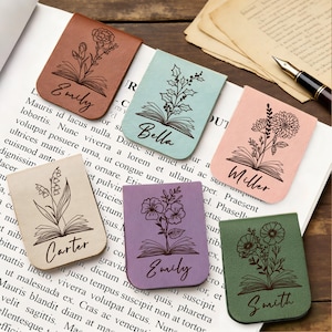 May include: A collection of leather bookmarks in various colors, each featuring a floral design and a name. The bookmarks are in shades of brown, green, purple, pink, and beige. The names are in a cursive font.