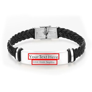 Op de afbeelding: Zwart leren armband met een zilveren sluiting en een rechthoekig zilveren label met de tekst "Your Text Here Love from Sophia".