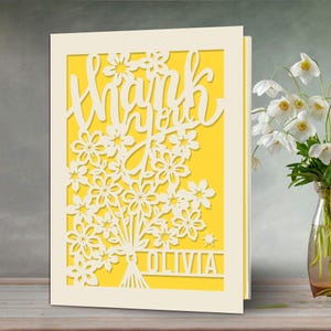 May include: A white card with a yellow background and a cut-out design of flowers and the words "Thank you Olivia".