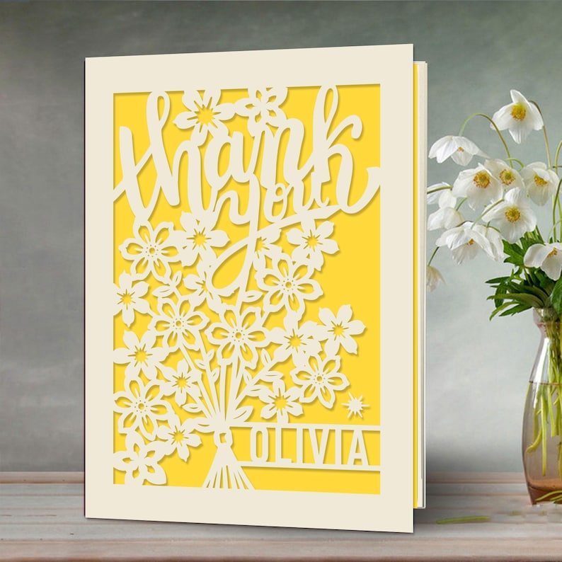 May include: A white card with a yellow background and a cut-out design of flowers and the words "Thank you Olivia".