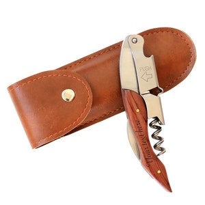 May include: A brown leather case with a silver and wood wine opener. The opener has a corkscrew, a bottle opener, and a foil cutter. The case has a snap closure. The opener is engraved with the text "Your text here".