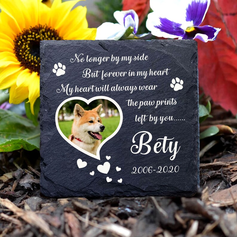 Puede incluir: Piedra conmemorativa de pizarra negra con una huella de pata blanca, un coraz&oacute;n y un texto que dice "No longer by my side But forever in my heart My heart will always wear the paw prints left by you...... Bety 2006-2020". Una foto de un perro est&aacute; en un marco en forma de coraz&oacute;n.