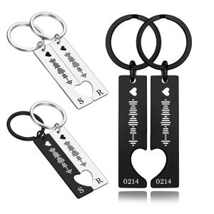 May include: Keychains with a heart-shaped cutout and a music waveform design. One keychain is black, the other is silver. Each keychain has a small heart and the initials "S" and "R". The black keychains have the numbers "0214" printed on them.