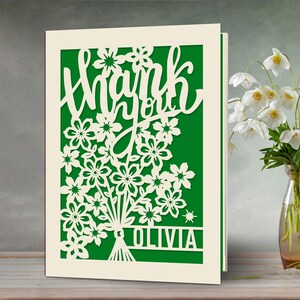 May include: A white card with a green background and a cut-out design of flowers and the words "Thank you Olivia".