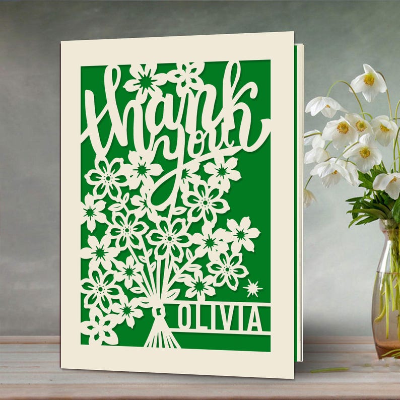 May include: A white card with a green background and a cut-out design of flowers and the words "Thank you Olivia".