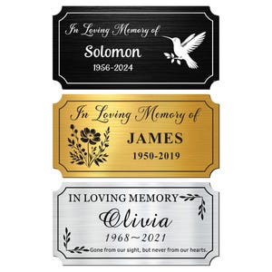 May include: Three memorial plaques with elegant designs. The top plaque is black with a hummingbird and the name "Solomon" and dates. The middle plaque is gold with a floral design and the name "James" and dates. The bottom plaque is silver with the name "Olivia" and dates.