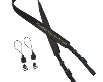 May include: Black leather camera strap with gold lettering that reads "Through the lens, See the World". The strap has two black adjustable clips.