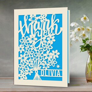 May include: A white card with a blue background and a cut-out design of flowers and the words "Thank you Olivia".