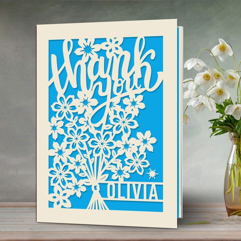 May include: A white card with a blue background and a cut-out design of flowers and the words "Thank you Olivia".