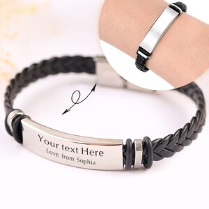 Op de afbeelding: Zwart gevlochten lederen armband met een zilveren metalen plaat waarop "Your text Here Love from Sophia" staat.