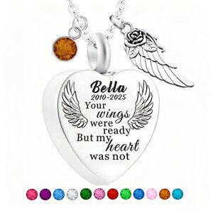 May include: A silver heart-shaped pendant necklace with the inscription "Bella 2010-2025 Your wings were ready But my heart was not." The necklace includes a charm with a rose and wing design, and a small orange gemstone. A row of colorful gemstones is at the bottom.