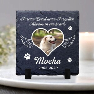 Puede incluir: Una placa conmemorativa de pizarra negra con un marco de foto en forma de coraz&oacute;n blanco, una huella de pata blanca y el texto "Forever Loved never Forgotten Always in our hearts". El marco de la foto contiene una imagen de un perro blanco. La placa tambi&eacute;n tiene el texto "Mocha 2006-2020" y dos huellas de patas blancas.