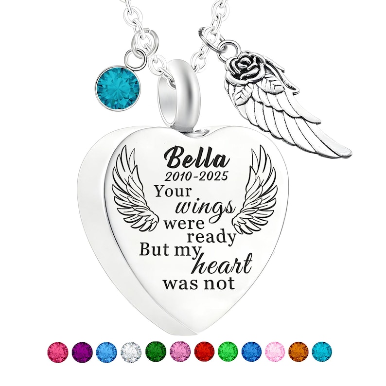 May include: A silver heart-shaped pendant necklace with the name "Bella" and dates "2010-2025" engraved on it. The pendant has a pair of wings and the words "Your wings were ready, But my heart was not". Includes a blue gemstone and a rose wing charm.
