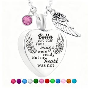 May include: A silver heart-shaped pendant necklace with a pink gemstone and a rose and wing charm. The pendant has the name "Bella" and the years "2010-2025" with the text "Your wings were ready But my heart was not."
