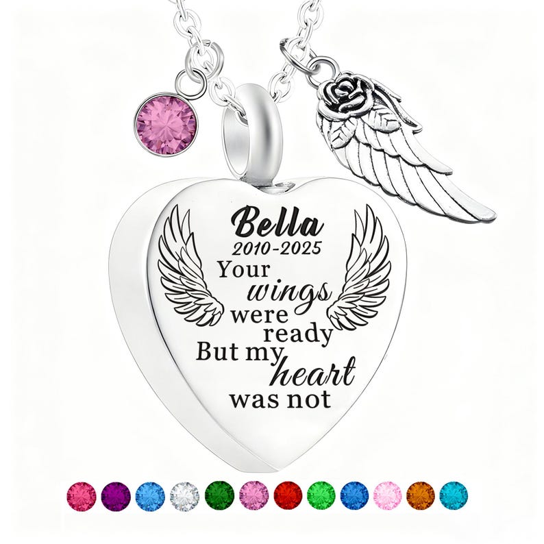 May include: A silver heart-shaped pendant necklace with a pink gemstone and a rose and wing charm. The pendant has the name "Bella" and the years "2010-2025" with the text "Your wings were ready But my heart was not."