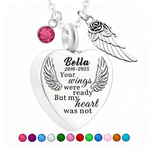 May include: A silver heart-shaped pendant necklace with the inscription "Bella 2010-2025 Your wings were ready But my heart was not." The necklace includes a pink gemstone, a rose and wing charm, and a selection of colorful gemstones.