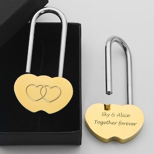 May include: Gold heart-shaped padlock with two interlocking hearts engraved on the front. The padlock is open and the shackle is extended. The shackle is engraved with the text "Sky & Alice Together forever".