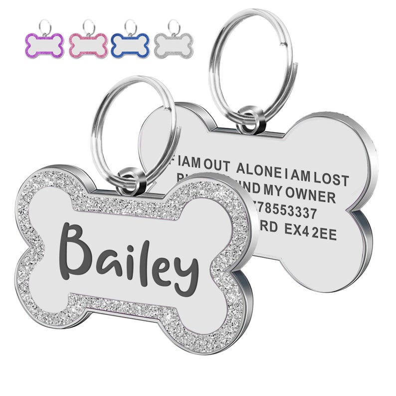 Op de afbeelding: Honden-ID-tag in de vorm van een bot met de naam "Bailey" in zwarte letters. De tag heeft een zilveren rand ingelegd met kleine, sprankelende kristallen. De tag bevat een zilveren ring voor bevestiging en de tekst "I AM OUT ALONE I AM LOST FIND MY OWNER 78553337 RD EX42EE".
