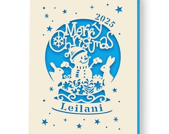 May include: A cream-colored Christmas card with a blue interior. The card features a cut-out design of a snowman, two rabbits, gifts, and the words "Merry Christmas 2025" and "Leilani". Blue stars and snowflakes are scattered around the design.