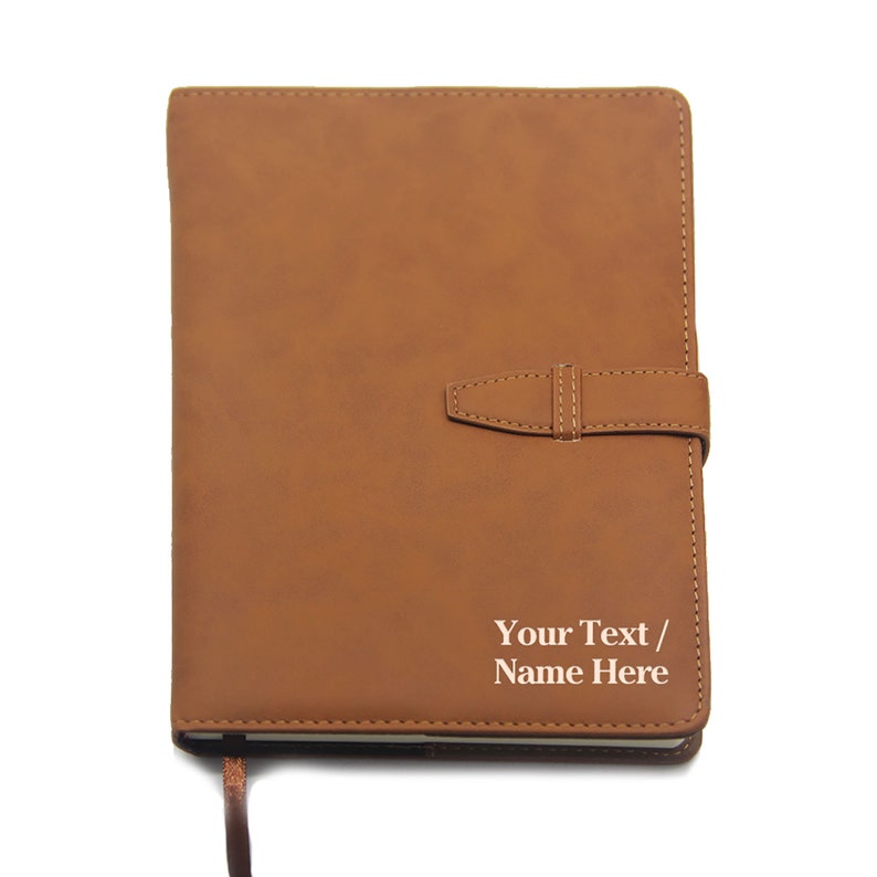 May include: A brown faux leather journal with a strap closure and a personalized inscription that reads "Your Text / Name Here".