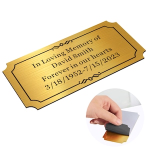May include: Gold-colored metal plaque with a decorative border and the text "In Loving Memory of David Smith Forever in our hearts 3/18/1952-7/15/2023"