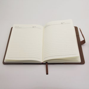 May include: A brown leather bound journal with a red ribbon bookmark. The journal has lined pages and a memo section on the front cover.