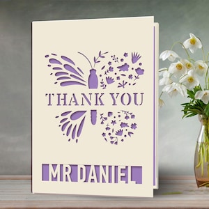 May include: A white card with a purple butterfly and floral design. The card says "Thank You" and "Mr. Daniel".