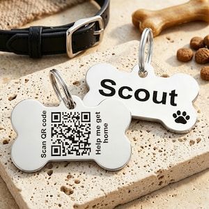 May include: Two silver-toned, bone-shaped pet identification tags with metal rings. One tag features the name Scout and a paw print. The other tag displays a QR code with the text Scan QR code and Help me get home engraved on the surface.