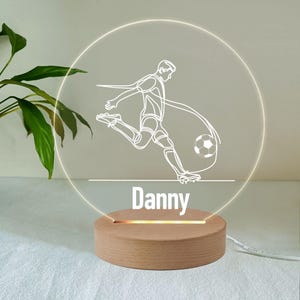 May include: A white LED night light with a wooden base. The light features a line drawing of a soccer player kicking a ball. The name "Danny" is written below the image.