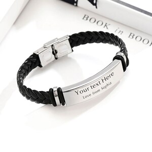 Op de afbeelding: Zwart leren armband met een zilveren metalen plaat gegraveerd met de tekst "Your text Here Love from Sophia".