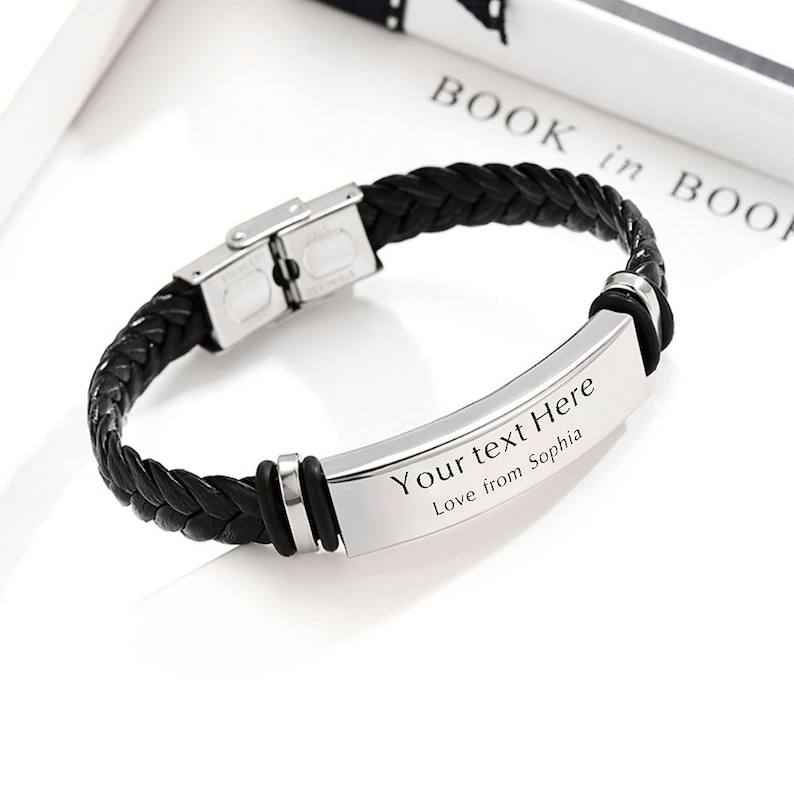 Op de afbeelding: Zwart leren armband met een zilveren metalen plaat gegraveerd met de tekst "Your text Here Love from Sophia".
