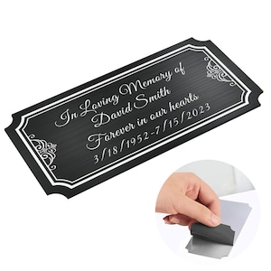 May include: Black memorial plaque with white lettering that reads "In Loving Memory of David Smith Forever in our hearts 3/18/1952-7/15/2023".
