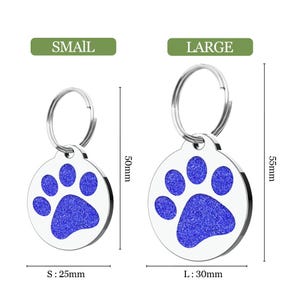Op de afbeelding: Twee roestvrijstalen huisdier-ID-tags, klein en groot, met een blauw pootafdrukontwerp. De kleine tag is 25 mm in diameter en 50 mm lang, terwijl de grote tag 30 mm in diameter en 55 mm lang is. De tags hebben een zilveren sleutelhanger.