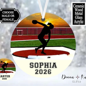 May include: A round ornament featuring a silhouette of a discus thrower on a track and field background. The text reads CHOOSE MALE OR FEMALE, CERAMIC WOOD METAL GLASS ACRYLIC, SOPHIA, and 2026. A smaller version shows the same design with the name CARTER.