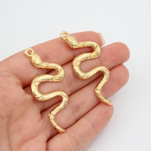 Op de afbeelding: Twee gouden slangenbedels met een getextureerd oppervlak. De bedels hebben de vorm van een slang die in een cirkel is opgerold.