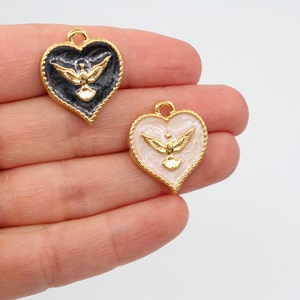 May include: Two gold heart-shaped charms with a gold dove design. One charm has a black enamel background and the other has a white enamel background.