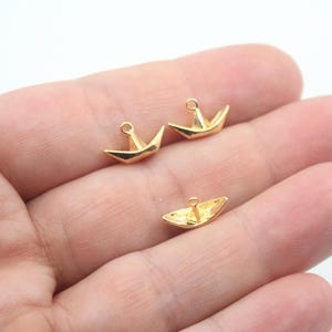 May include: Three gold-colored paper boat charms with a loop for attaching to jewelry or other crafts.