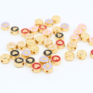 May include: A collection of gold-colored round beads with a heart design. The beads are in various colors, including pink, red, black, and white.