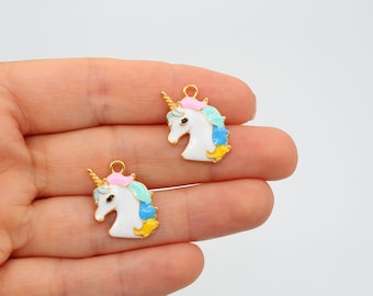 Op de afbeelding: Twee gouden unicorn-bedels met wit emaille en kleurrijke accenten. De unicorn-bedels hebben een roze, blauwe en gele manen en staart.