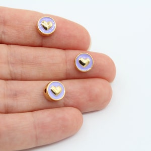 May include: Three gold-colored round beads with a lavender enamel coating and a gold heart design.