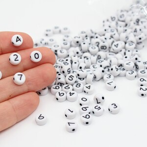 May include: White plastic beads with black numbers from 0 to 9. The beads are scattered on a white surface.