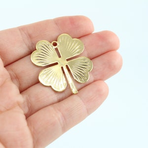 May include: Gold-colored metal four-leaf clover charm with a textured surface.