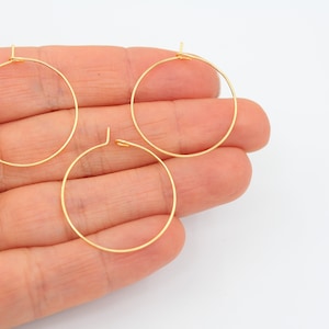 May include: Three gold-coloured hoop earrings of different sizes. The hoops are made of thin wire and are open at the top.