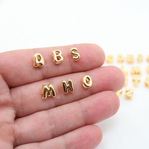 Könnte beinhalten: Goldene Buchstabenperlen im Alphabet A, B, S, M, H, O. Die Perlen sind klein und rund, perfekt für die Schmuckherstellung oder andere Bastelarbeiten.